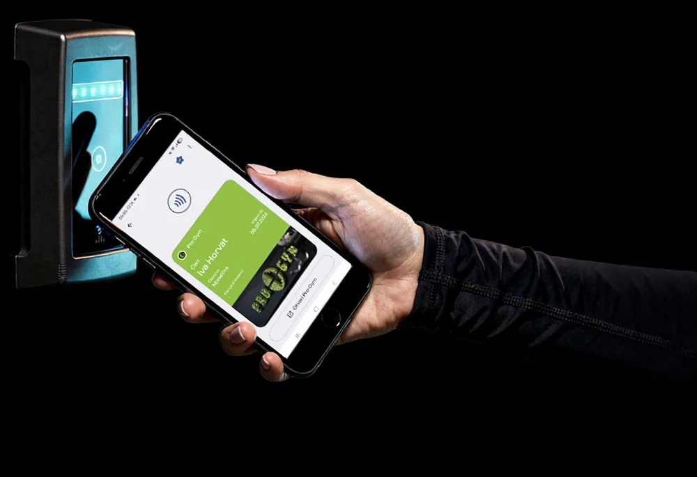 Ruka prislanja telefon sa zelenom Pro-Gym članskom karticom u walletu na čitač na ulazu u teretanu.